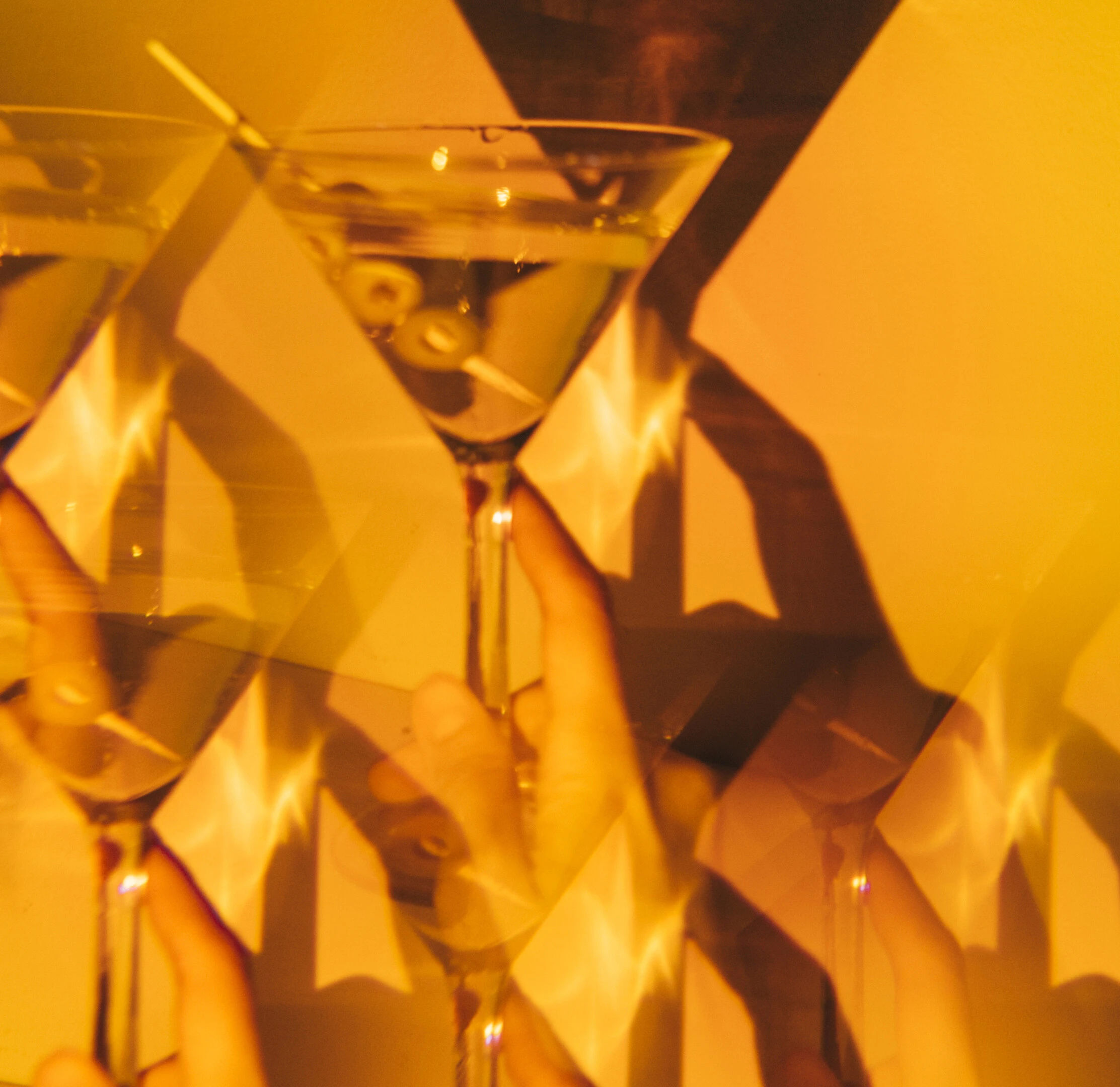 Verre de martini Gorda aux olives tenu à la main, reflets superposés sous lumière ambre de gala