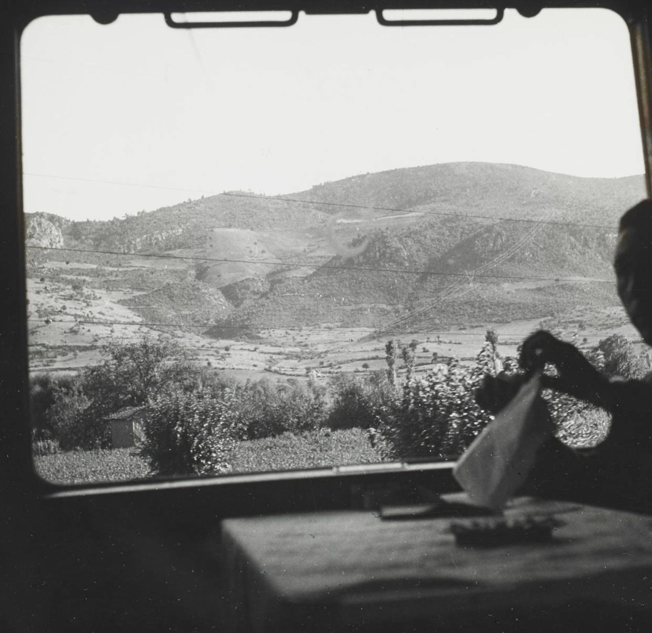 Passager de l'Orient Express dépliant une serviette à table, vue depuis la fenêtre du wagon sur collines et champs